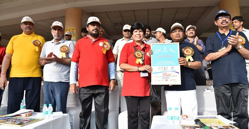 Officials in caps and event T-shirts on a stage in New Delhi, holding up a printed poster at the flag-off of the 16th Run against Drug Abuse.